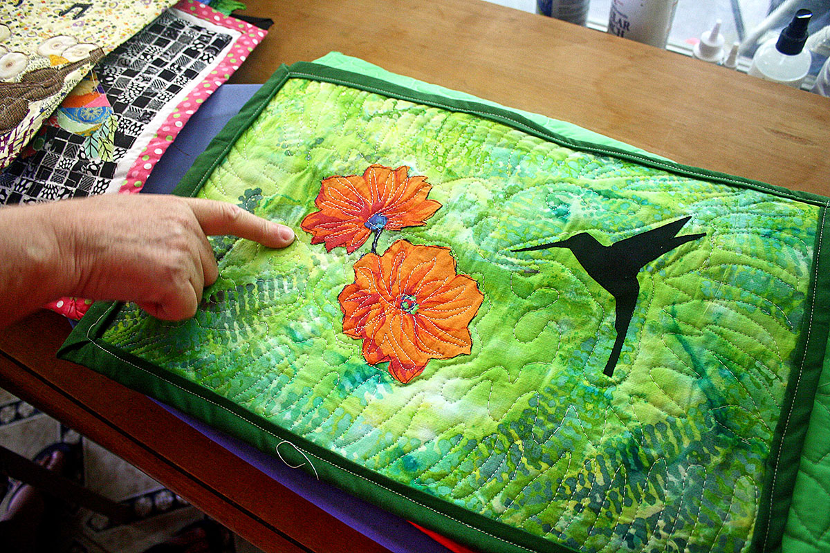 Laffont’s subject choices reflect her deep concern for the environment. In this quilt, you can see the intricate free-form quilting lines that accentuate the flower applique and mimic the fern pattern of the fabric.