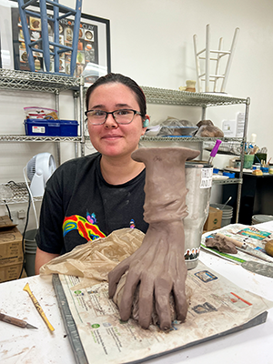 Pottery student Mia Iken, 16, loves sculpture. The arm and hand clutchinga round object is her first sculpture at this studio.