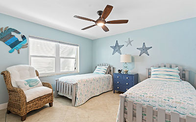 This breezy coastal-themed guest bedroom features twin beds with matching quilts with fish from top to bottom.