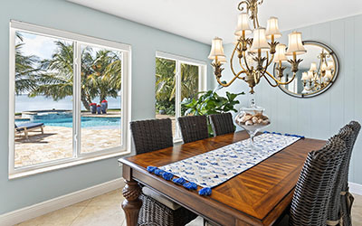 The pale blue walls and ample windows of the intimate dining room make for an airy and charming space. The ornate chandelier, formal wooden table and rattan chairs complete the setting.