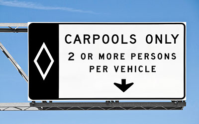 Overhead freeway carpool only sign with blue sky.