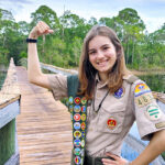 Determined to become one of the rare Eagle Scouts in the Boy Scouts of America, soon to be known as Scouting America, Charlotte Arlidge stands on the Spruce Bluff bridge before her Eagle Scout project to replace railings began. Many of her 65 merit badges are visible.